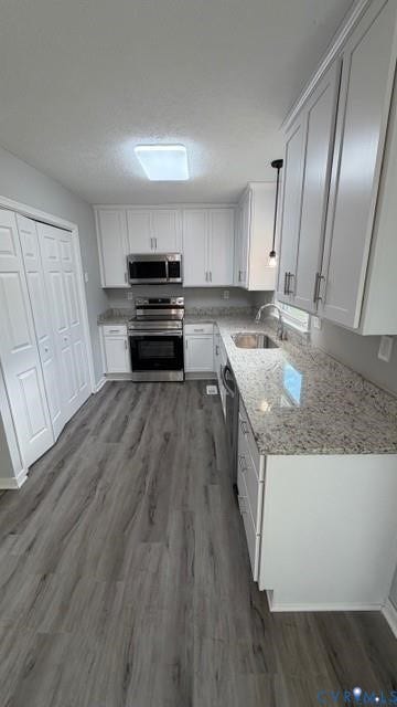 White shaker-style cabinetry, stainless steel appliances, light-toned granite countertops, wood-finish flooring, and a stainless steel sink