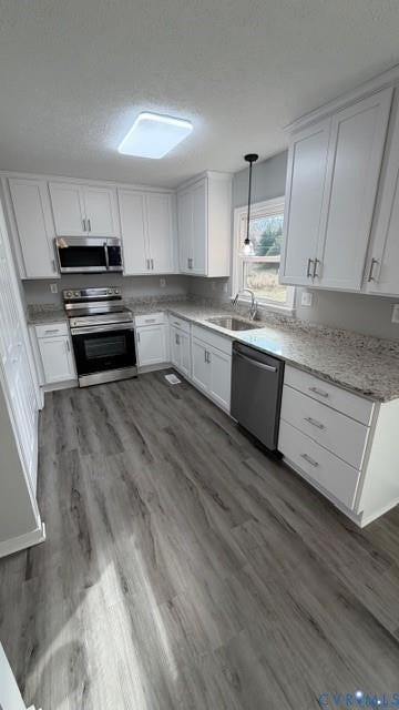 Kitchen featuring white shaker cabinetry, stainless steel appliances, speckled countertops, and wood-finish flooring