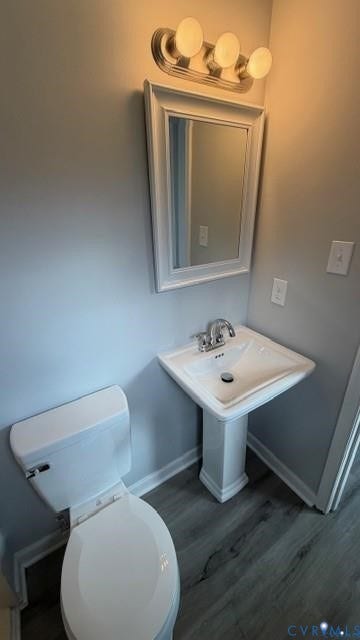 Pedestal sink with chrome faucet, classic white toilet, vanity mirror with sconce lighting, and wood-finish flooring