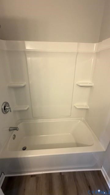 White bathtub with an integrated shower surround, chrome fixtures, and built-in shelving