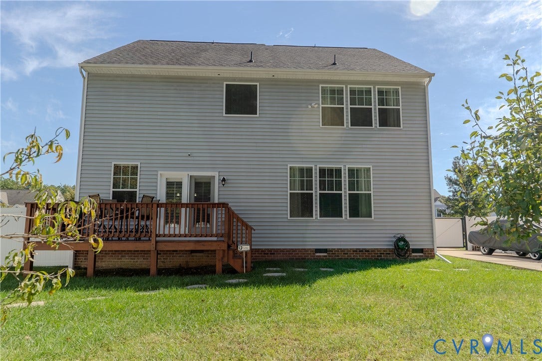 Two-story residence with light gray siding, a brick foundation perimeter, multiple paneled windows, and a raised wooden deck with a balustrade