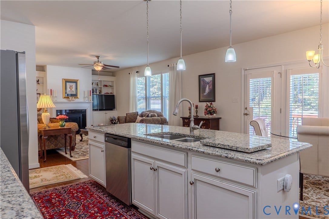 Kitchen featuring a central island with stone countertop, undermount double-basin sink, stainless steel dishwasher, white cabinetry, and overhead pendant lighting