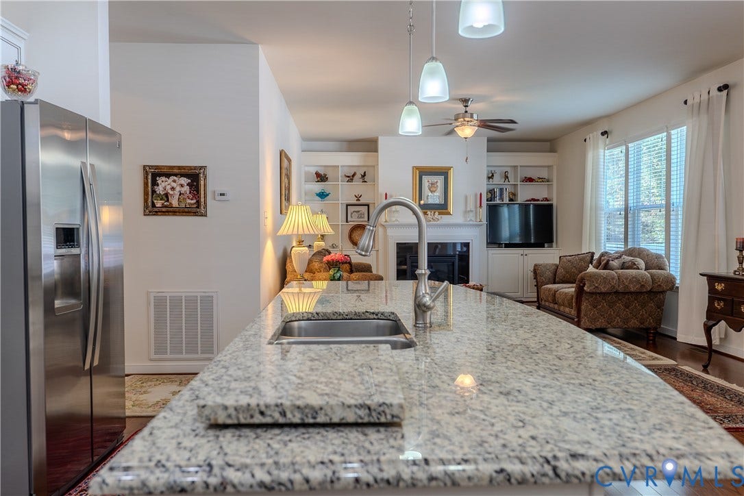 Kitchen featuring a stone-topped island with an undermount sink, stainless steel refrigerator, built-in shelving, and a fireplace with a decorative mantel