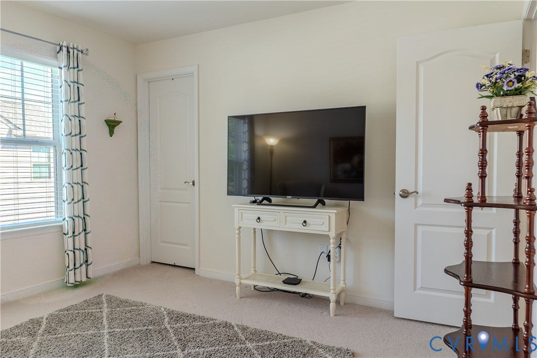 Neutral-toned room featuring wall-to-wall carpeting, two arched-panel interior doors, and a double-hung window with a brushed-nickel curtain rod