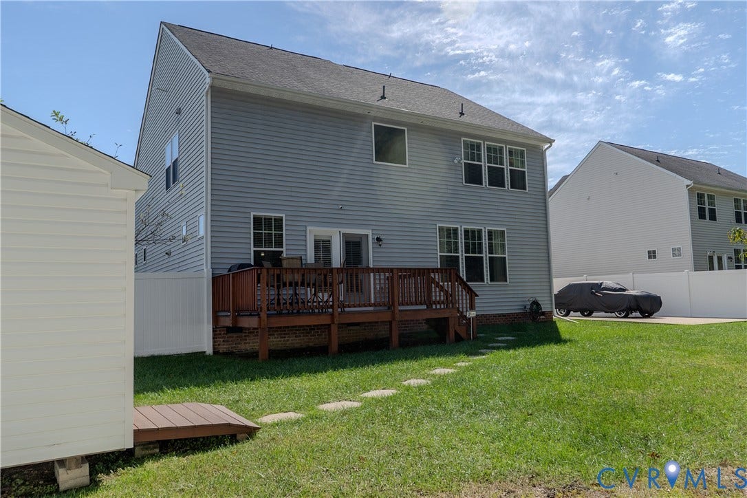Two-story residence featuring light gray siding, an elevated wood deck, a rear lawn, and white privacy fencing