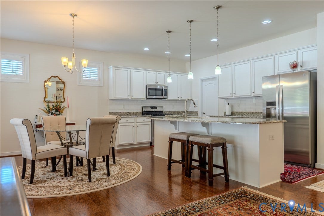 Kitchen featuring white cabinetry, stone countertops, stainless steel appliances, a center island with pendant lighting, and wood-finish flooring