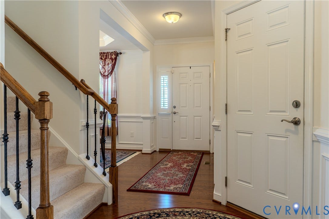 Foyer featuring wood-finish flooring, wainscoting, a six-panel entry door with sidelight, and a staircase with a wood handrail and iron balusters