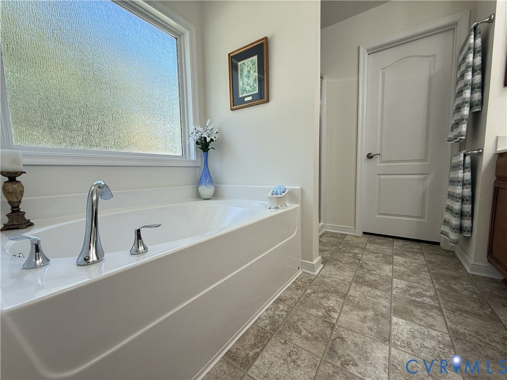 Soaking tub with chrome faucet fixtures, frosted window, and neutral-tone tile flooring