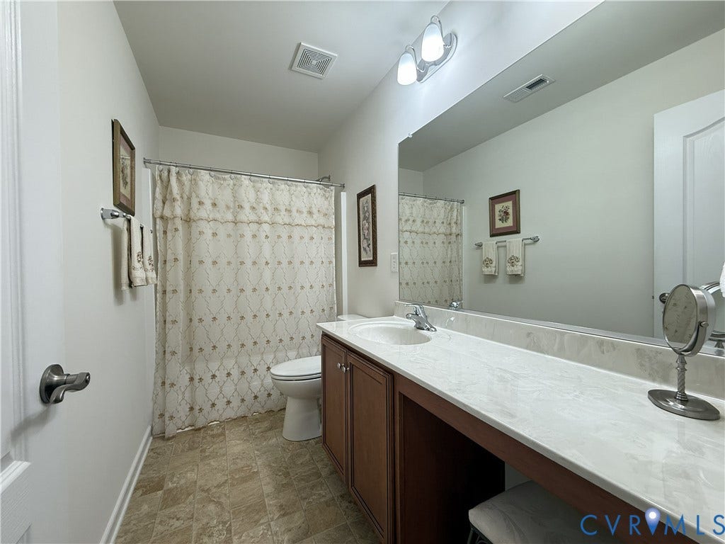 Bathroom featuring a vanity with stone-finish countertop, undermount sink, wood-finish cabinetry, full-width wall mirror, and tile flooring