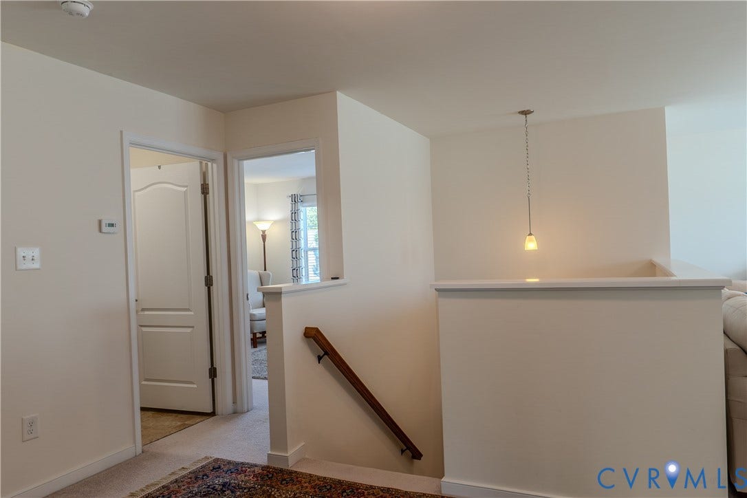 Neutral wall color, single-panel interior doors, low-profile pendant lighting, carpeted flooring, and a wooden handrail