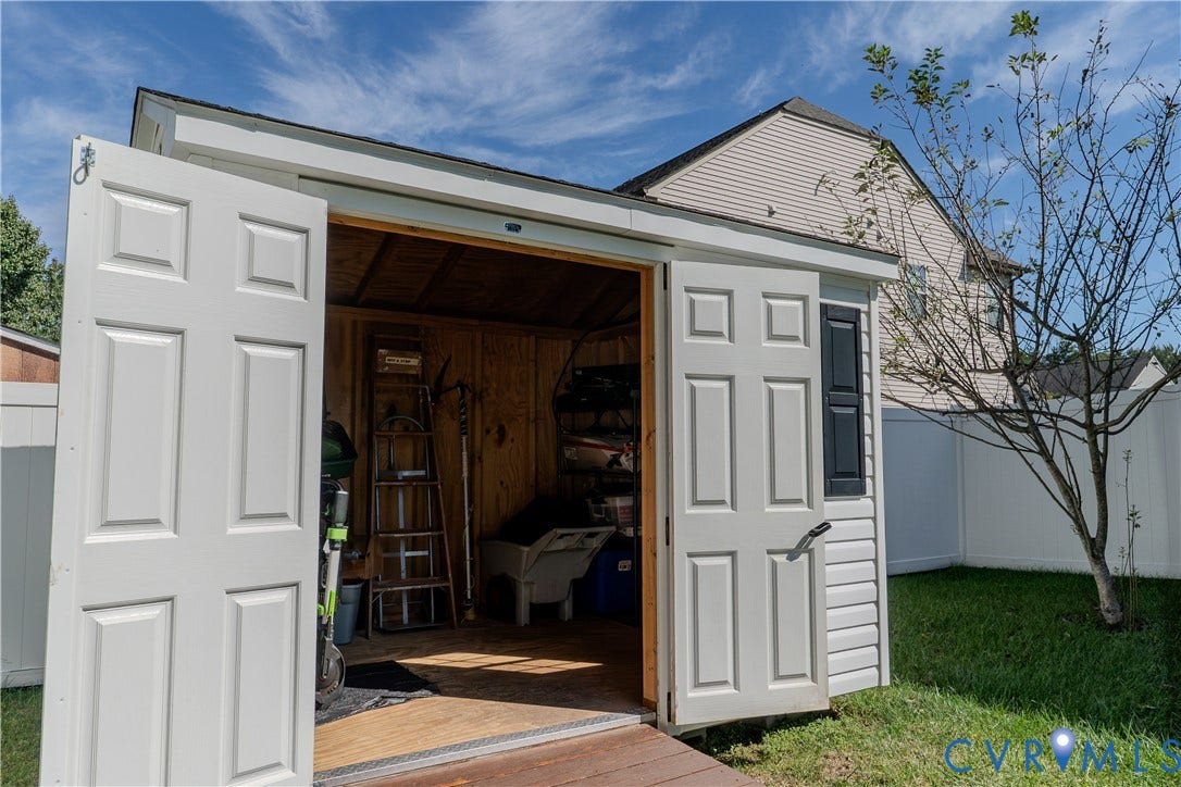 Storage shed featuring dual swinging doors, vinyl siding, shutter accents, and wood-panel interior walls