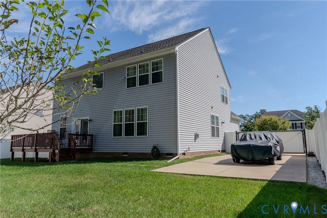 Two-story residence featuring light gray vinyl siding, a rear wood deck, a concrete parking pad, and a perimeter vinyl fence