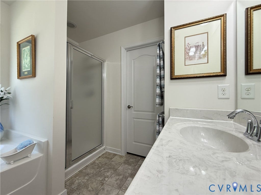 Bathroom featuring a vanity with a white-veined countertop, an oval undermount sink, a chrome faucet, a stall shower with a metallic frame, and tile flooring
