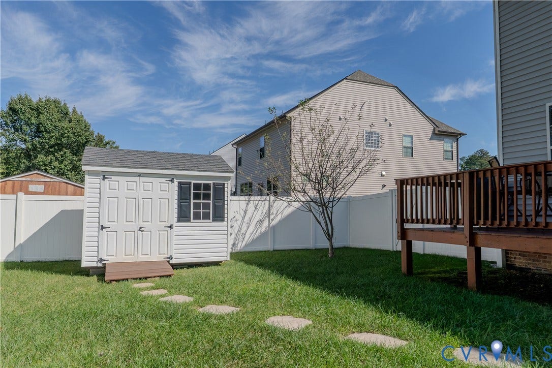 Backyard featuring a wood-tone deck, white vinyl privacy fencing, a storage shed with double doors, and stone paver path