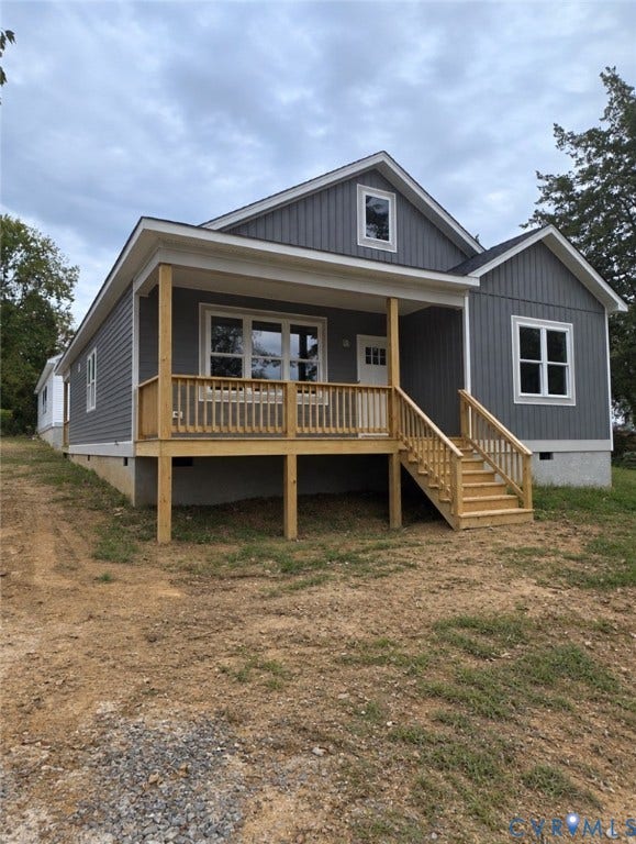 Single-story exterior featuring vertical gray siding, a covered wooden front porch with railing, a gable roofline, and multi-pane windows