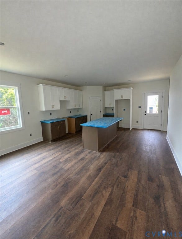 Kitchen featuring white upper cabinetry, dark base cabinetry, center island, and wood-finish flooring