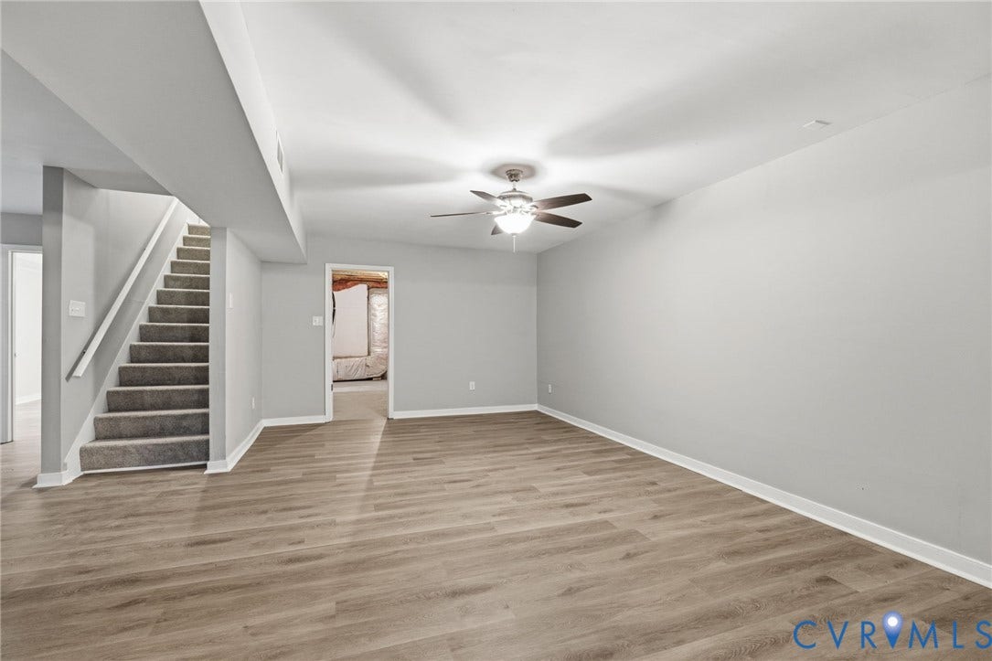 10731 Spring Run Road, Manchester, Chesterfield, VA 23832 Spacious room with wood-finish flooring, ceiling fan with light fixture, white baseboards, and a carpeted staircase