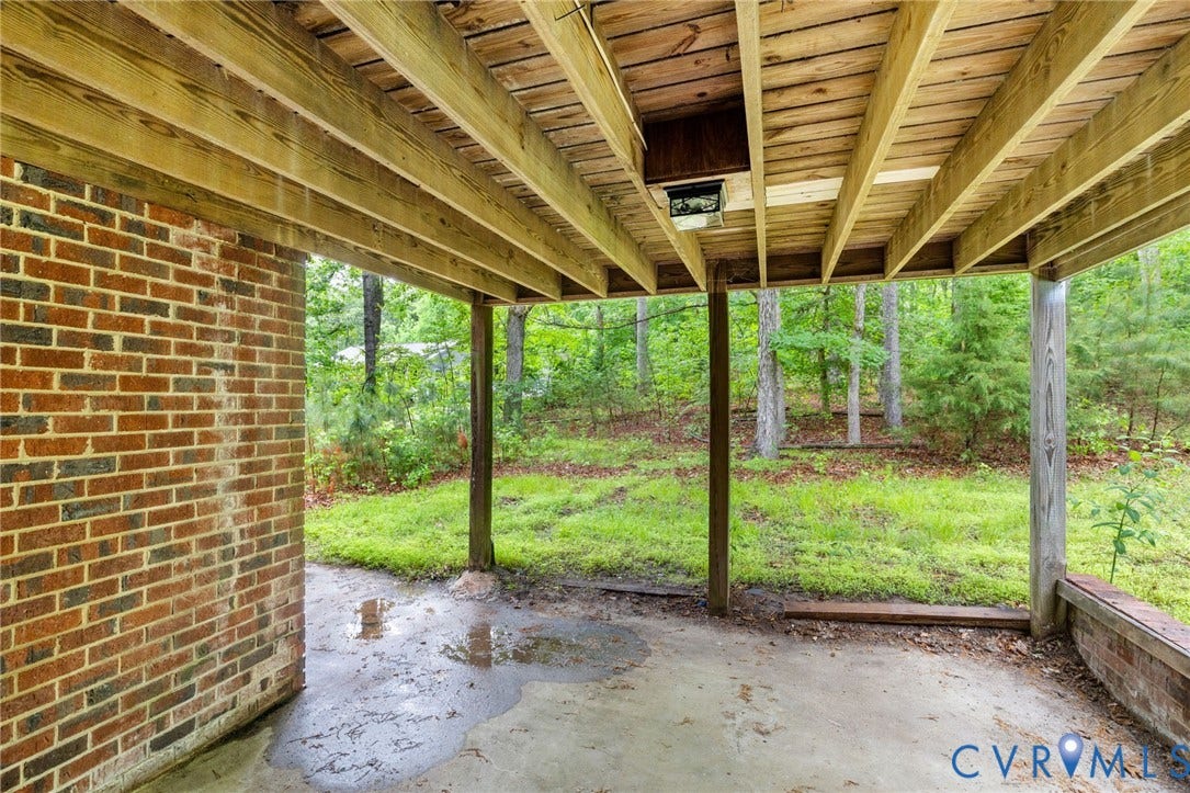 10731 Spring Run Road, Manchester, Chesterfield, VA 23832 Covered concrete patio with a brick wall and a wooded backdrop