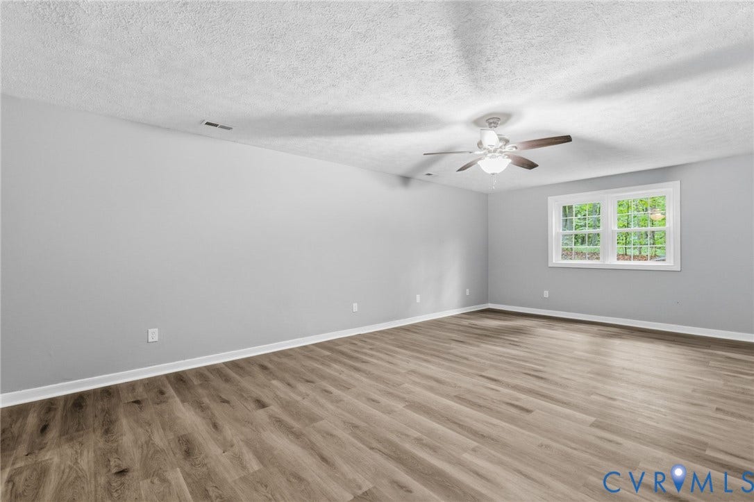 10731 Spring Run Road, Manchester, Chesterfield, VA 23832 Spacious room featuring wood-finish flooring, light gray walls, a window with white trim, and a ceiling fan with integrated lighting
