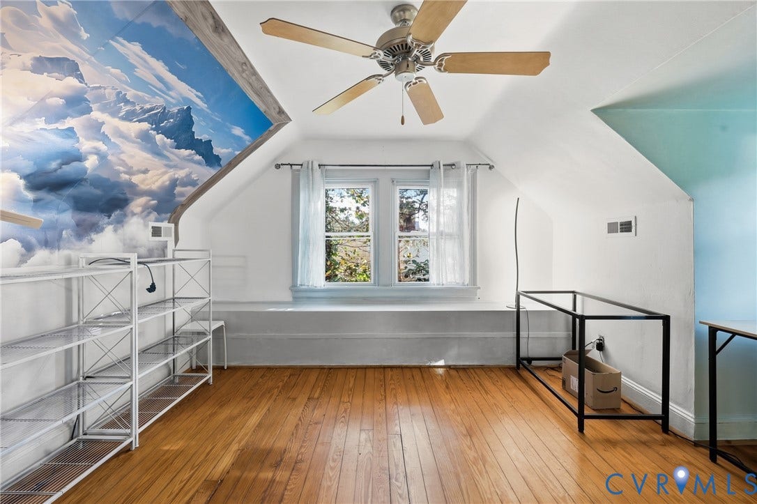 Attic space featuring wood-finish flooring, a ceiling fan, and a painted accent wall