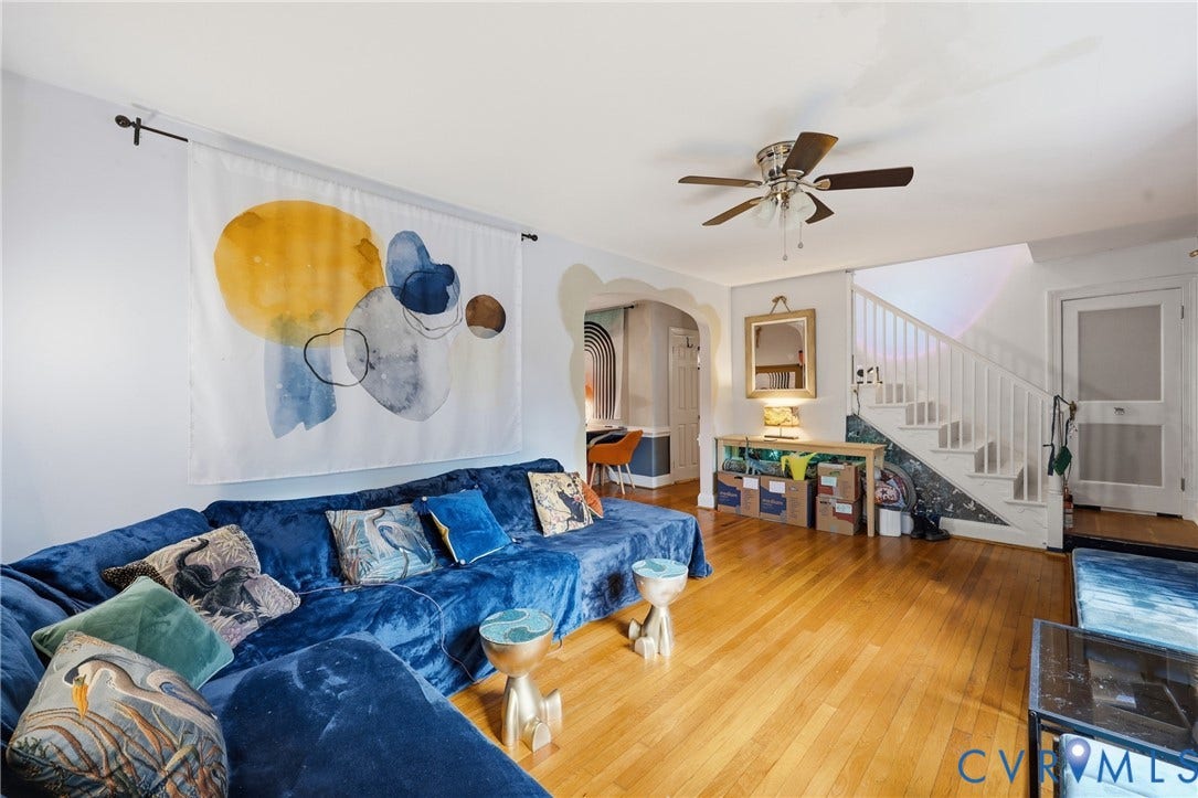 Hardwood flooring throughout, ceiling fan with integrated lighting, and a white staircase with spindle railings