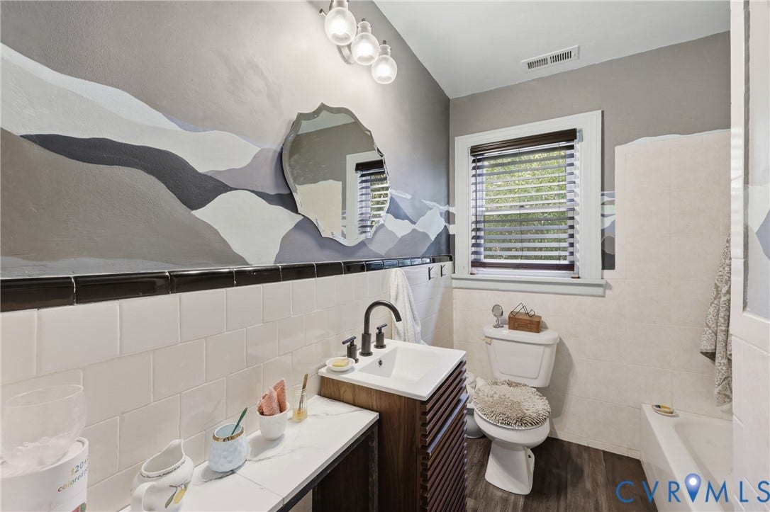 Modern vanity with a vessel sink and dark wood-finish cabinet, white subway tile wainscoting, decorative wall mirror, and wood-look flooring
