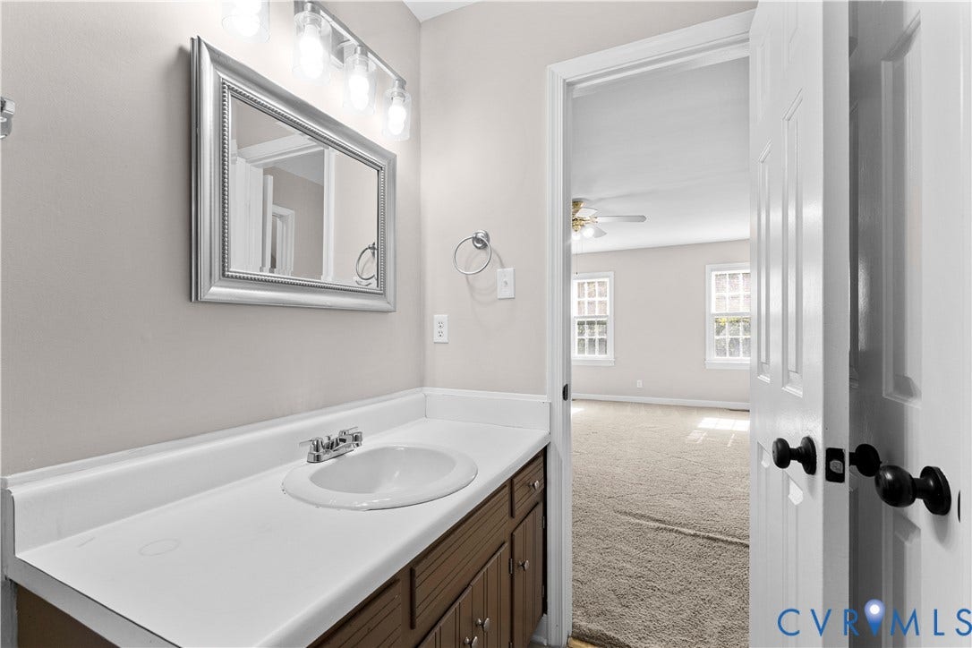 2307 Garrison Place Terrace, Garrison Place, Midlothian, VA 23112 Vanity featuring a white countertop with an integrated basin, wood-finish cabinetry, framed wall-mounted mirror, and multi-bulb light fixture