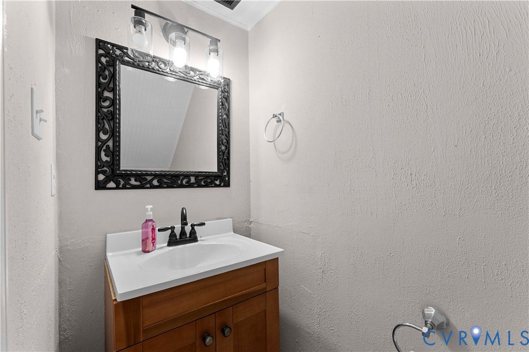2307 Garrison Place Terrace, Garrison Place, Midlothian, VA 23112 Wood-finish vanity with an integrated basin, decorative black-framed mirror, three-light fixture with clear glass shades, and matte black dual-handle faucet