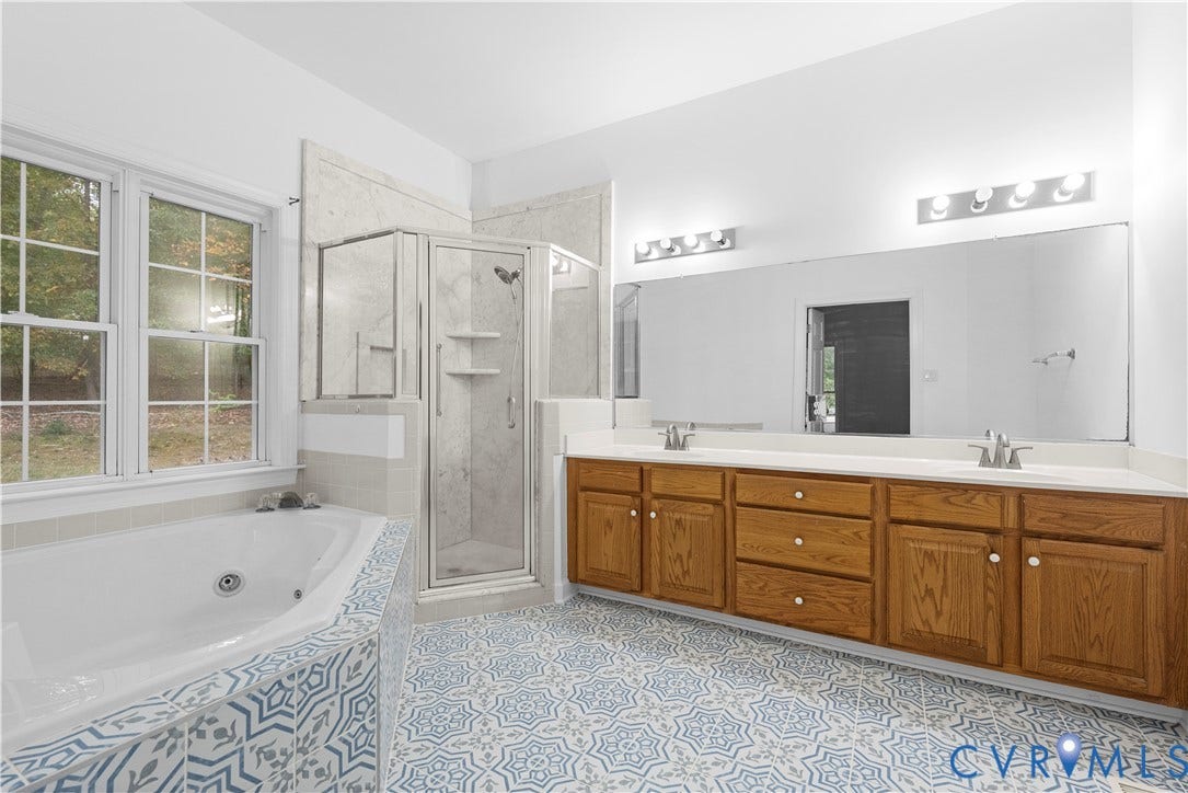 3437 Riverton Court, Robious Road Corridor, Midlothian, VA 23113 Dual-sink vanity with wood-finish cabinetry, corner soaking tub, glass-enclosed shower, patterned tile flooring, and a full-width wall mirror