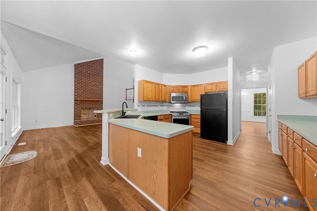 3437 Riverton Court, Robious Road Corridor, Midlothian, VA 23113 Kitchen featuring wood-finish cabinetry, countertop peninsula, and integrated appliances, set against a vaulted ceiling and exposed brick fireplace