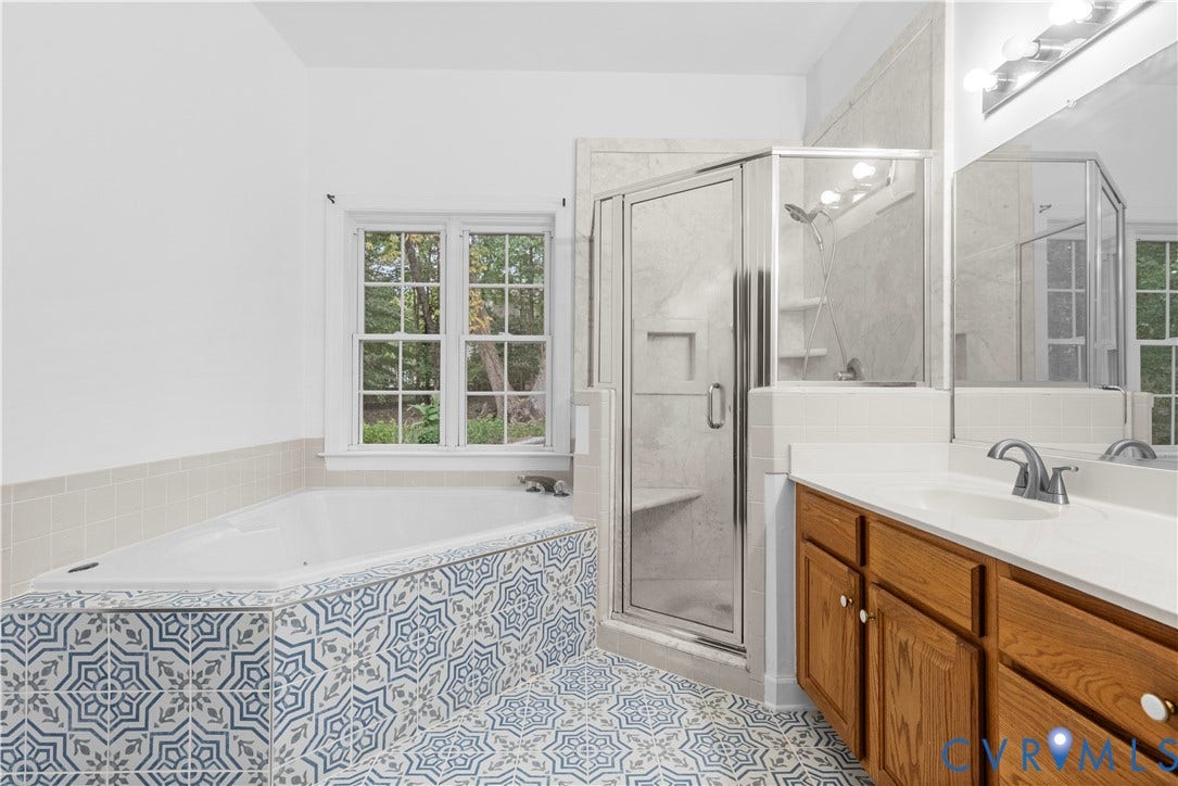 3437 Riverton Court, Robious Road Corridor, Midlothian, VA 23113 Bathroom featuring a jetted tub with patterned tile surround, walk-in glass shower with stone-finish walls, double-door wood cabinetry, and large-format wall mirror