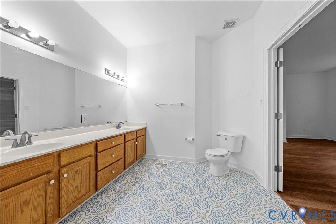 3437 Riverton Court, Robious Road Corridor, Midlothian, VA 23113 Dual-sink vanity with wood-finish cabinetry, countertop-integrated sinks, full-width vanity mirror, multi-bulb wall lighting, and patterned tile flooring