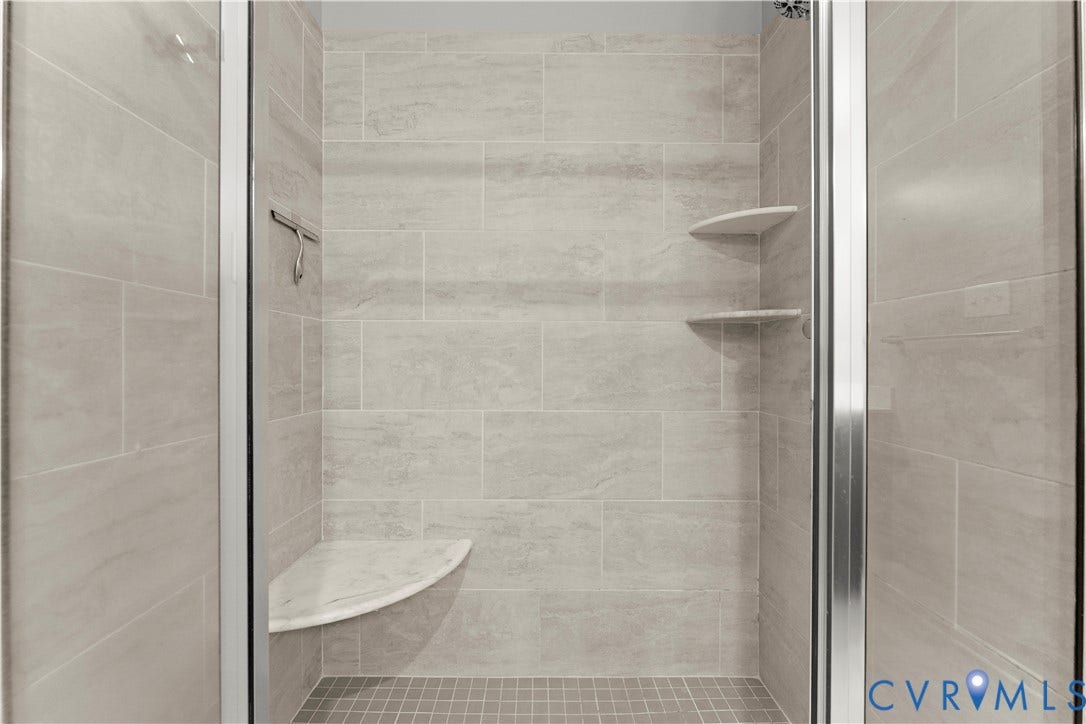 2953 Preston Park Court, Western Goochland County, Goochland, VA 23153 Shower enclosure featuring glass doors with chrome hardware, full-height tile surround, built-in corner shelving, and a built-in bench