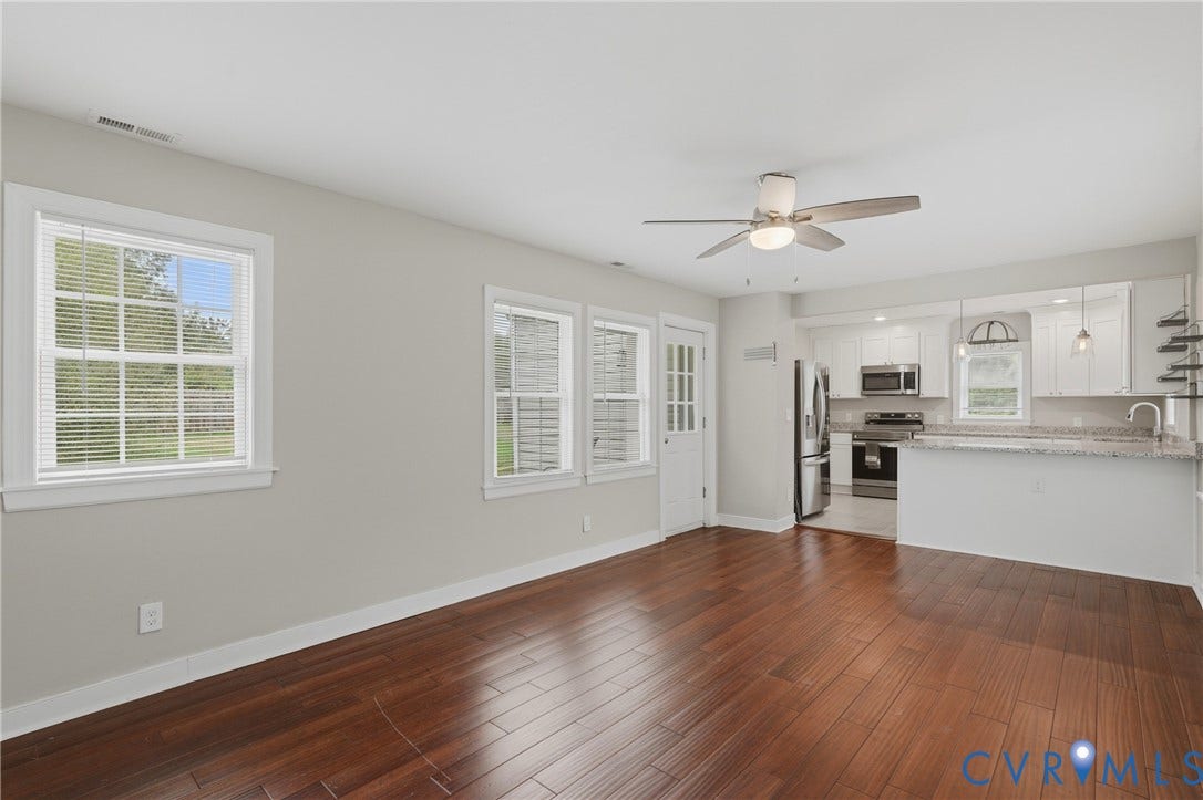 6624 Miller Road, Henrico, VA 23231 Open-concept living space with rich engineered bamboo flooring, abundant natural light from multiple windows, ceiling fan with integrated lighting, and seamless access to a modern kitchen featuring stainless steel appliances, white cabinetry, and a peninsula eat-in counter