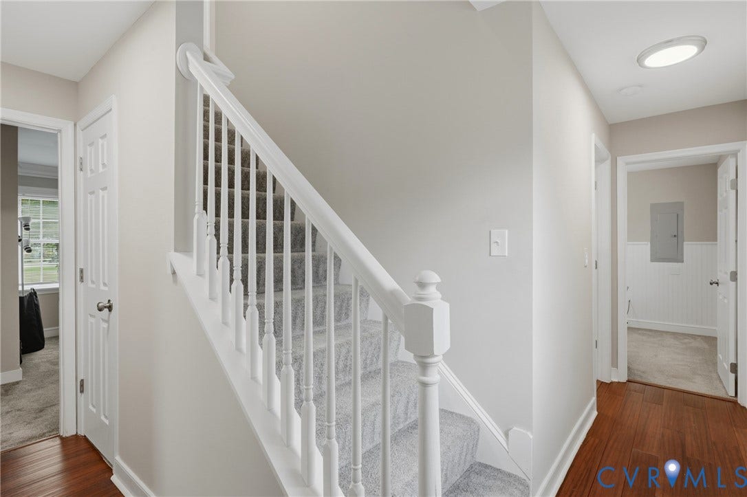 6624 Miller Road, Henrico, VA 23231 Elegant staircase featuring white painted spindles and railings with a polished newel post, complemented by warm wood-finish flooring and neutral wall finishes