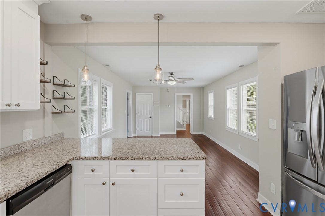 6624 Miller Road, Henrico, VA 23231 The modern kitchen features white cabinetry with brushed nickel hardware, granite countertops, stainless steel appliances, and pendant lighting over the island. This view shows the open connection to the living room.