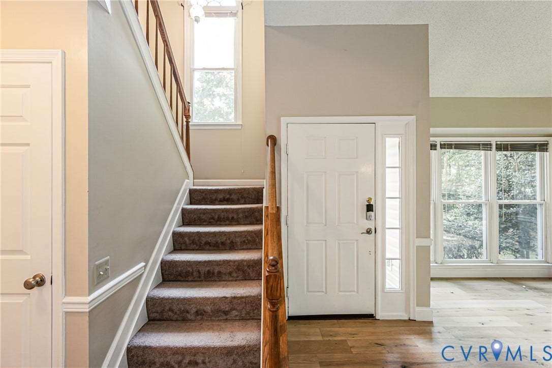Hardwood flooring, paneled entry door with sidelight, natural wood stair railing, carpeted stairs, and crown molding accents