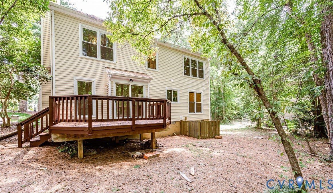 Expansive rear deck with wooden railings, siding exterior, multiple windows, and a wooded backdrop