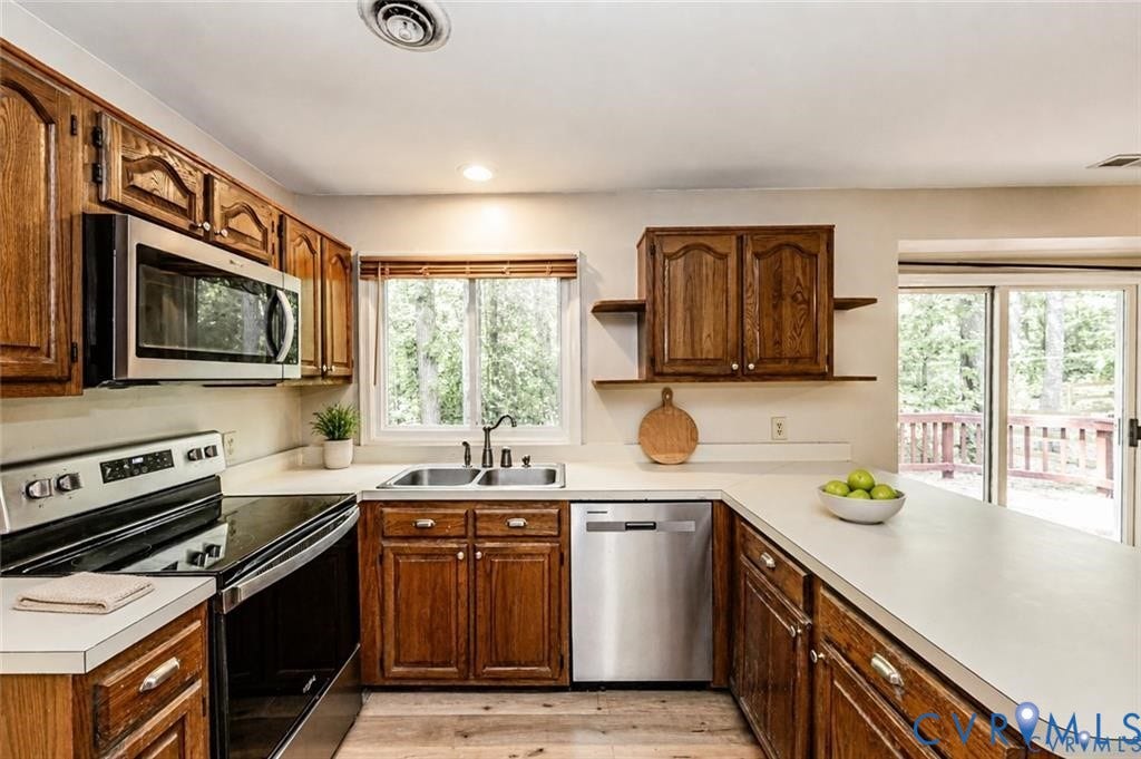 Kitchen featuring wood cabinetry, stainless steel appliances, a double basin sink, light-toned countertops, and wood-finish flooring