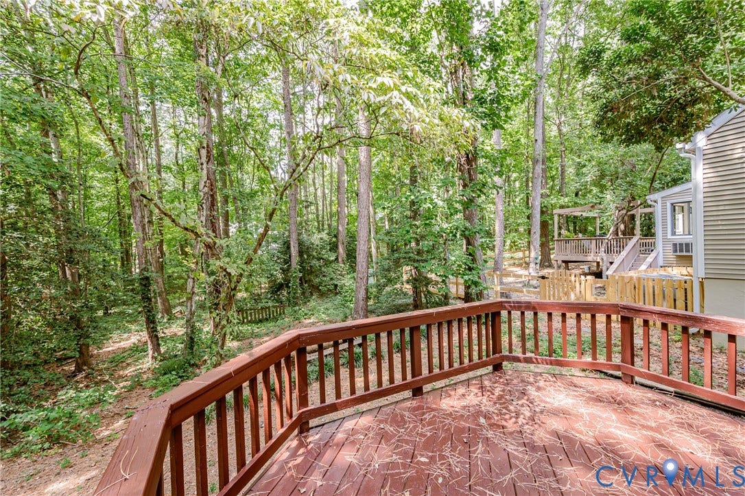 Expansive wood deck with a perimeter railing, surrounded by mature trees
