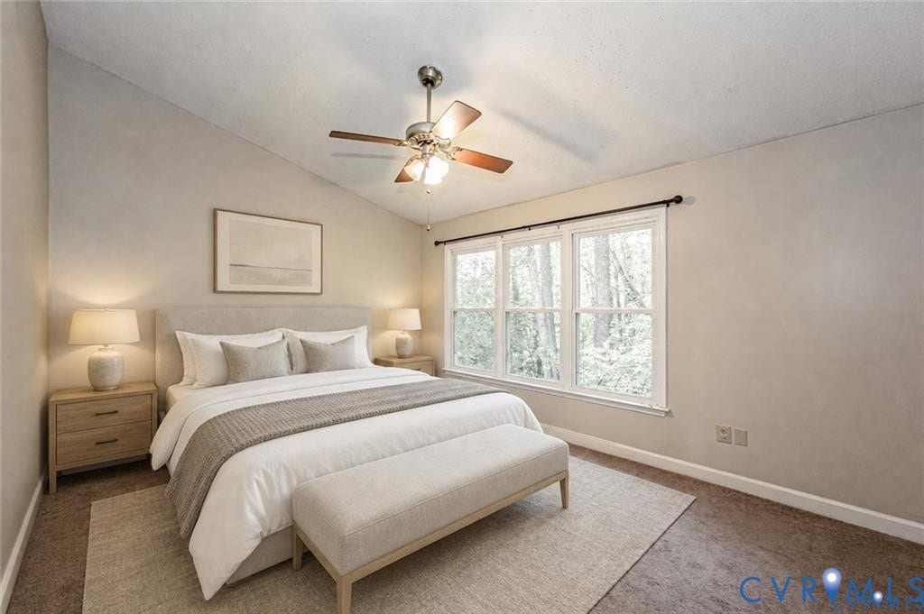 Vaulted ceiling with a ceiling fan, three pane windows, and neutral carpeting