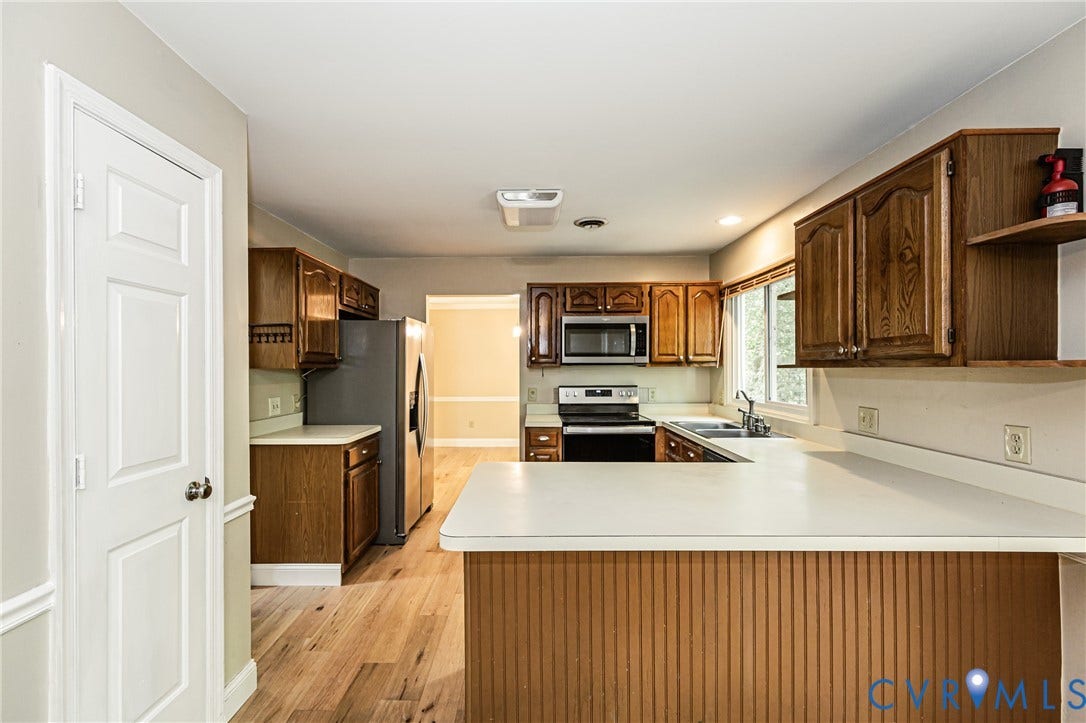 Kitchen featuring wood-finish flooring, white countertops, wood cabinetry, and stainless steel appliances
