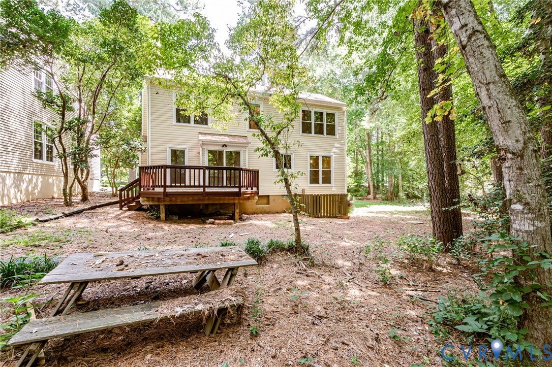 Expansive wooded backyard featuring a multi-level deck with wood railing, tan siding, and multiple windows