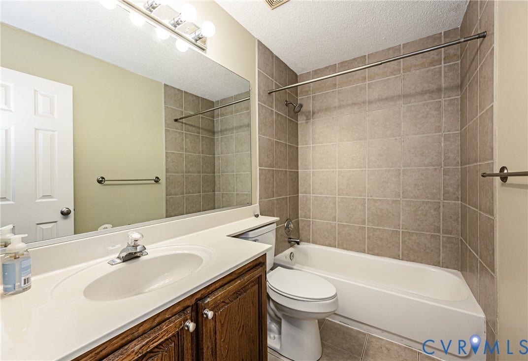 Bathroom featuring a shower-tub combination with tiled surround, a vanity with an integrated sink and wood-finish cabinetry, and a full-width mirror