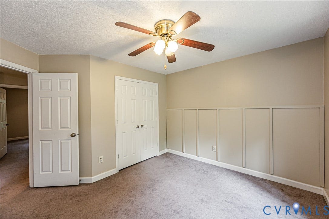 Neutral wall paint, ceiling fan with light kit, panel molding accent wall, six-panel interior doors, and carpet flooring