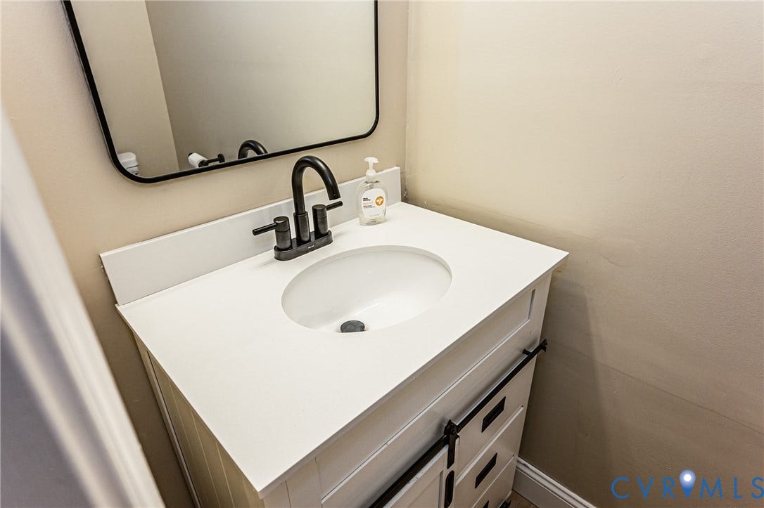 White vanity with a single basin sink, matte black faucet, and rectangular mirror