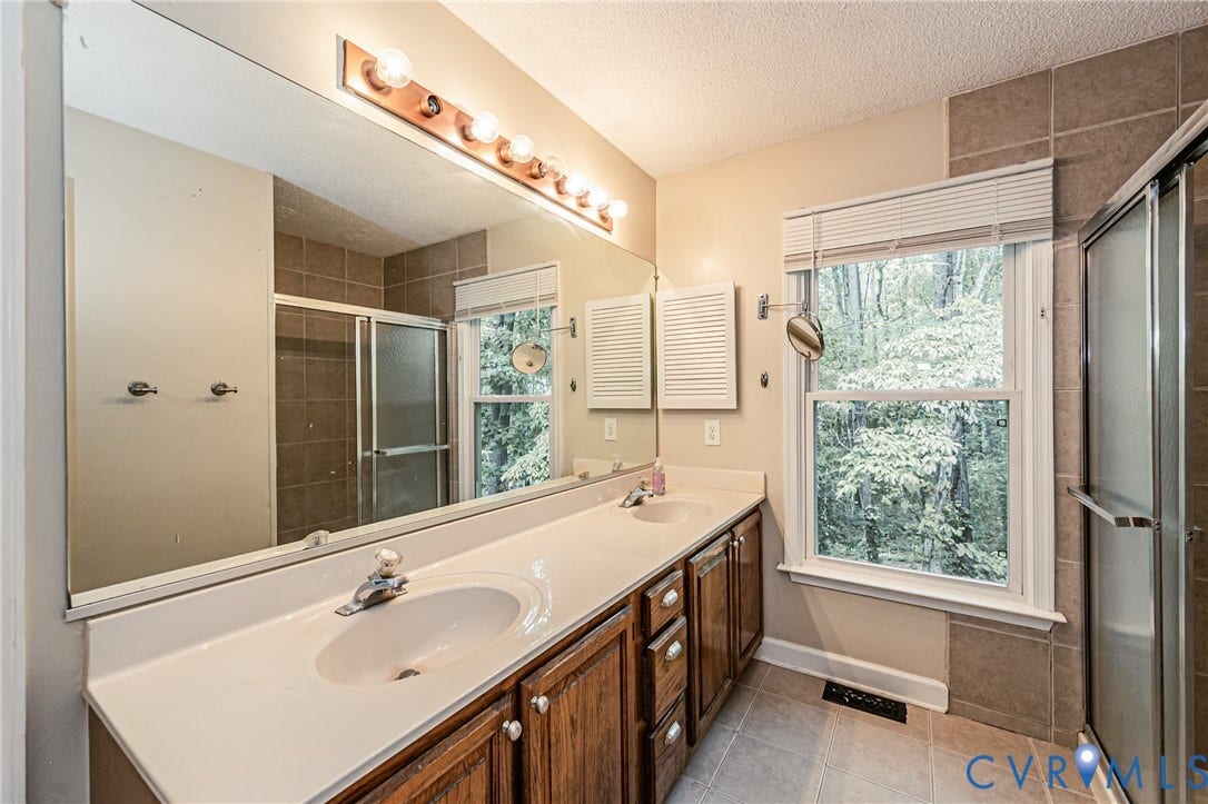 Dual vanity with integrated sinks, wood-finish cabinetry, full-width mirror, and a tiled shower enclosure