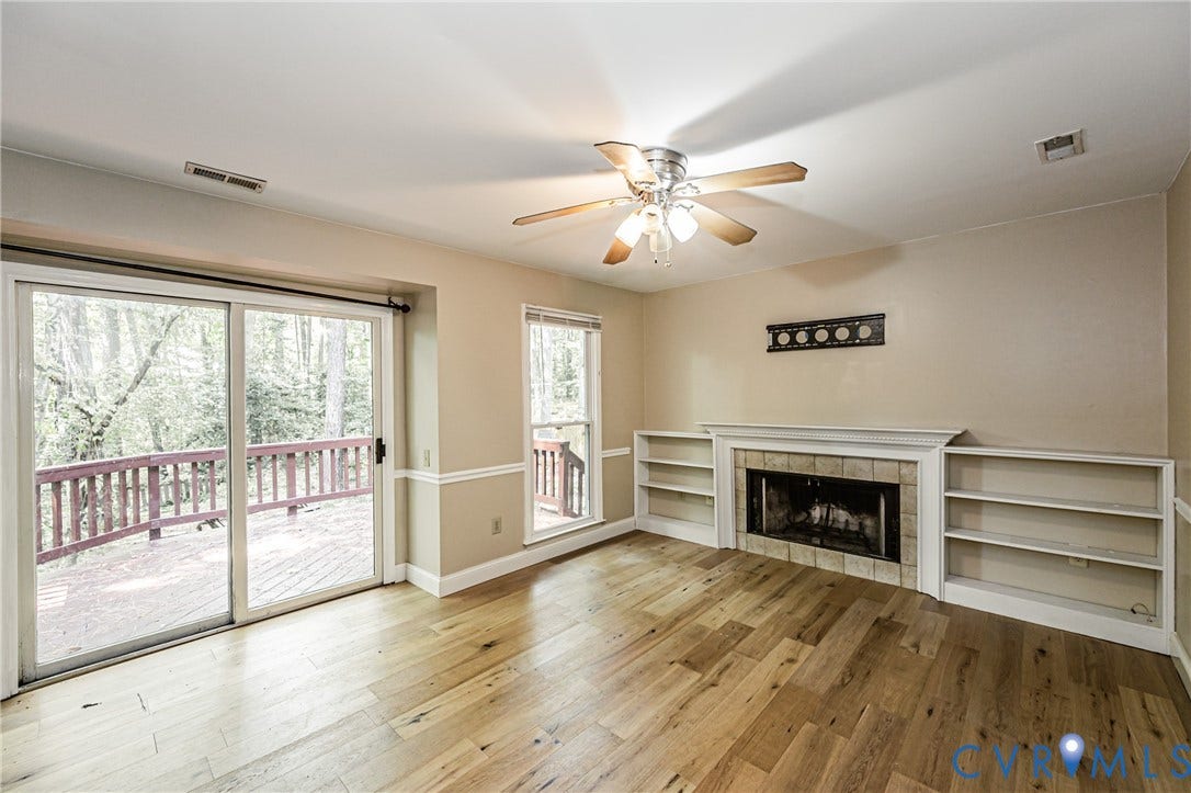 Hardwood flooring, fireplace with tile surround, built-in shelving, ceiling fan, and sliding glass door to exterior deck