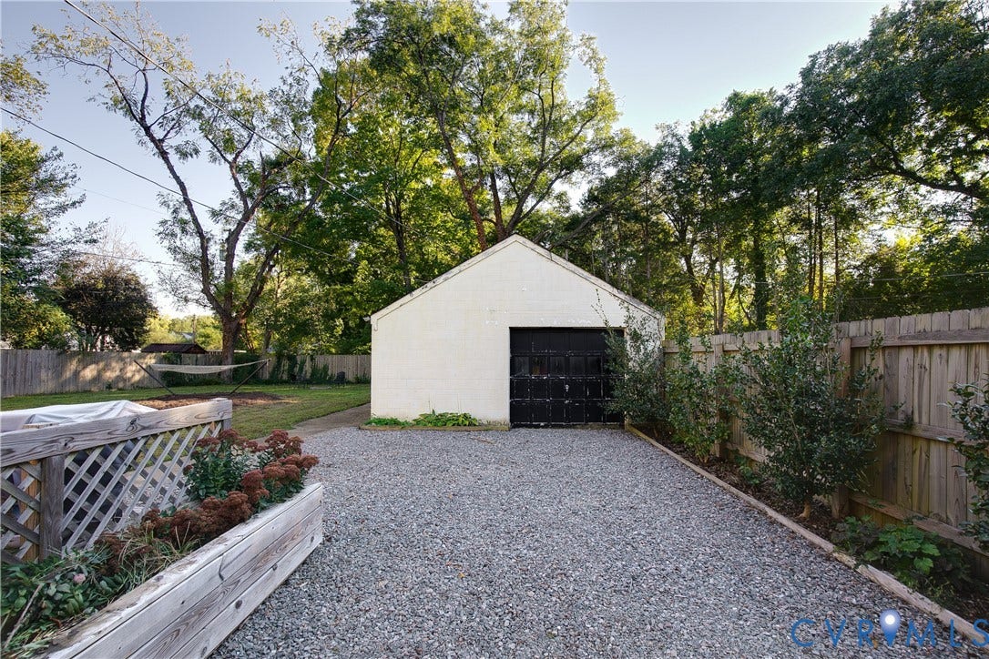 2207 Locbury Lane, Henrico, VA 23228 Detached masonry garage with a single-bay overhead door, gravel driveway, wood perimeter fencing, and raised timber garden beds