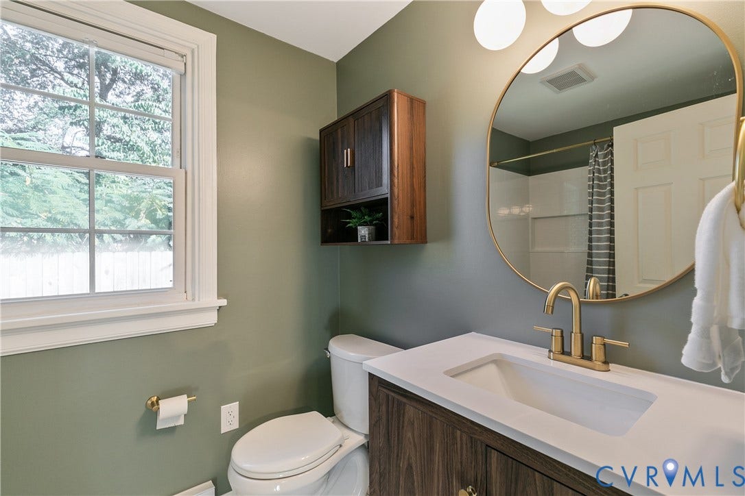 2207 Locbury Lane, Henrico, VA 23228 Wood-finish vanity with a stone countertop, integrated undermount sink, brass-toned faucet, matching wall-mounted medicine cabinet, and a circular gold-rimmed mirror
